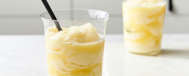 Two modern glasses filled with fresh squeezed frozen lemonade with black spoons in a beautiful white marble kitchen