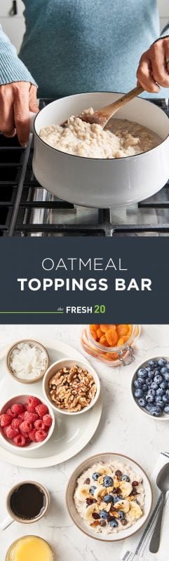 Woman stirring a fresh batch of oatmeal in a white pot with a bowl of oatmeal & a variety of toppings with coffee on a white marble surface