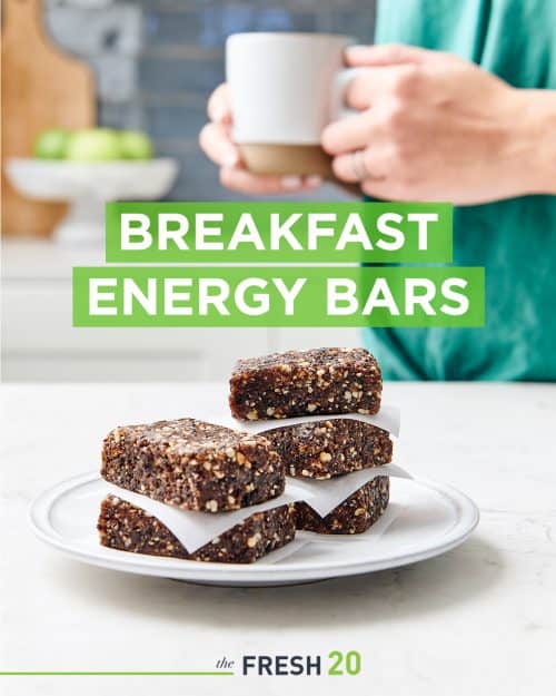 No bake breakfast energy bars stacked on a ceramic plate in front of a woman with a cup of tea in a beautiful white marble kitchen