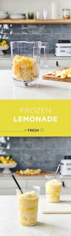 Blender full of fresh lemons & pineapple in a beautiful white marble kitchen with 2 modern glasses of frozen lemonade with lemons on a wood cutting board