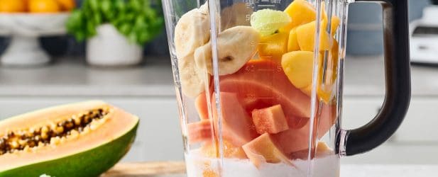 Blender full of fresh mango, bannanas, & papaya in a beautiful white marble kitchen