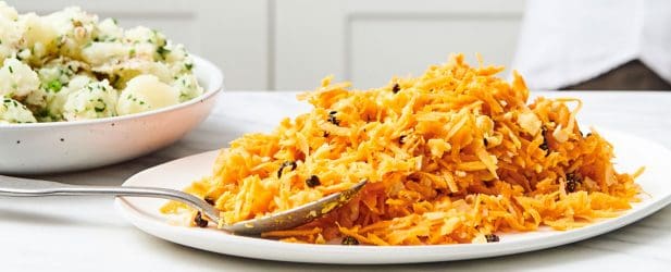 Vibrant rich orange carrot slaw on a cream colored plate in a white marble kitchen