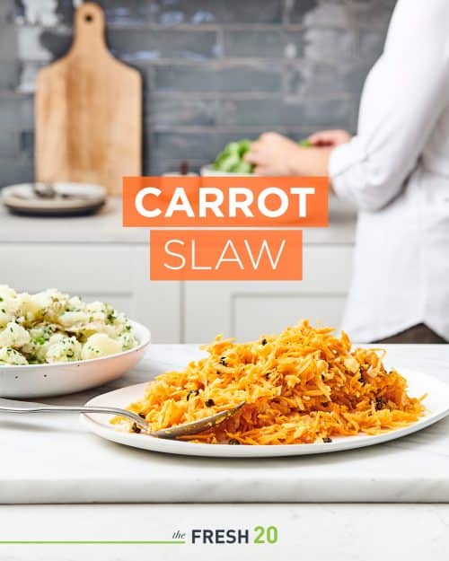 Vibrant carrot slaw with raisins on a ceramic plate with a serving spoon in a white marble kitchen