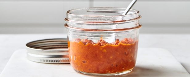 Mini mason jar filled with red hot Asian DIY homemade hot sauce in a white marble kitchen