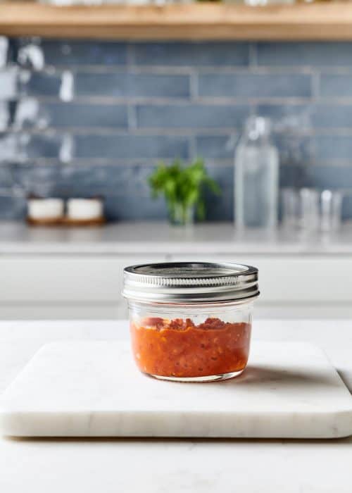 Mini mason jar filled with red hot Asian DIY homemade hot sauce in a white marble kitchen