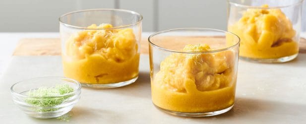 Three mini glass cups filled with quick & easy mango sorbet with lime zest in a white marble kitchen