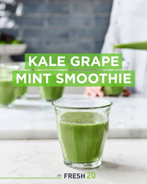 Woman making a glass of morning kale grape mint smoothie in a white marble kitchen