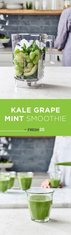 Woman filling a blender full of green grapes, mint, kale, lime & avocados & a small glass in a white marble kitchen