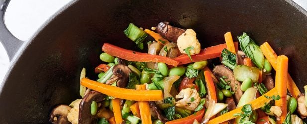 Le Creuset wok filled with vibrant 8 vegetable stir-fry on a white marble surface with linen napkin