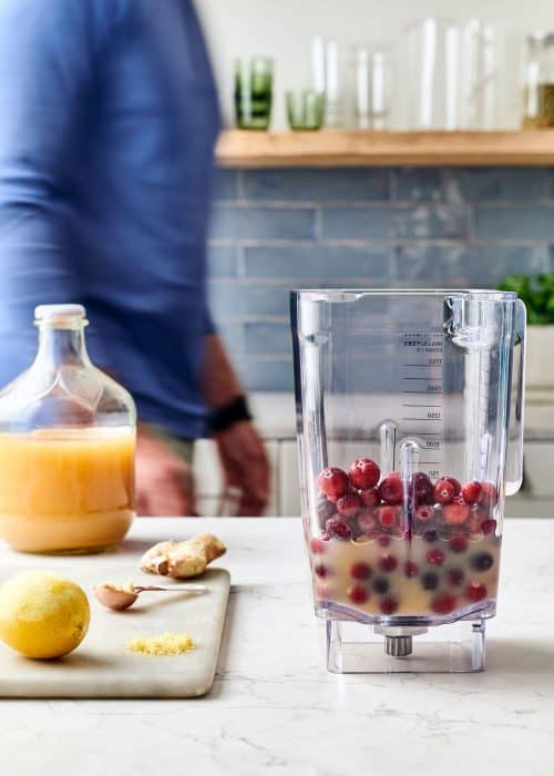 Man making a blender full of cranberries, apple juice and lemon zest in a white marble kitchen