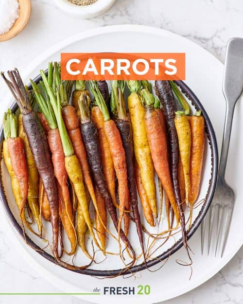 Colorful orange yellow and purple roasted carrots with their tops in a white ceramic bowl