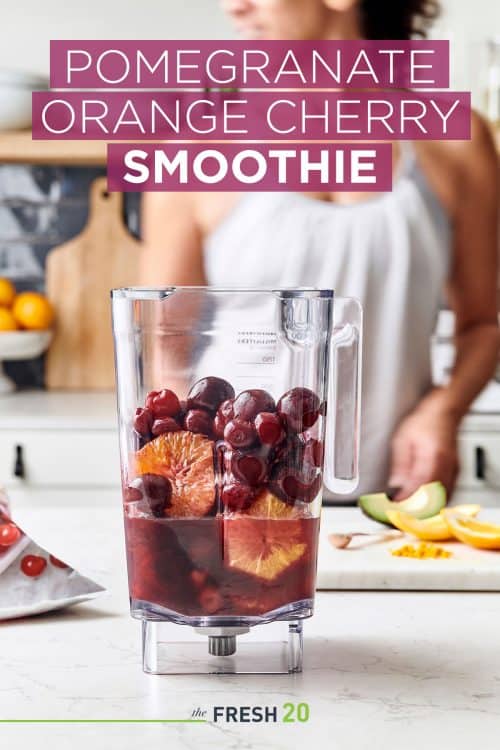 Woman making a blender full of pomegranate juice, oranges, cherries & avocado on a white marble surface in a beautiful kitchen