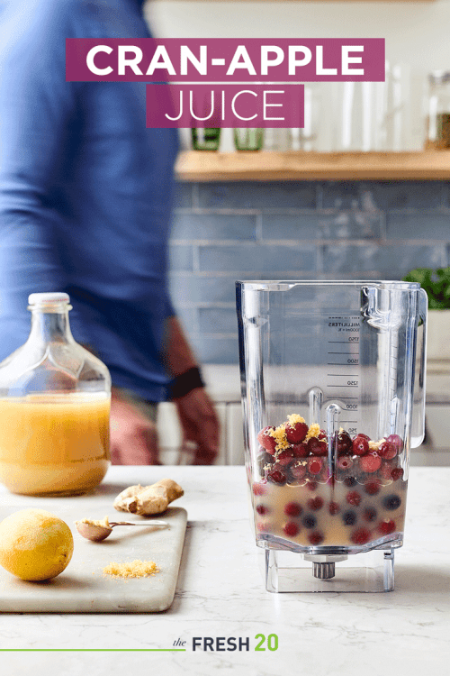 Man making a blender full of cranberries, apple juice and lemon zest in a white marble kitchen