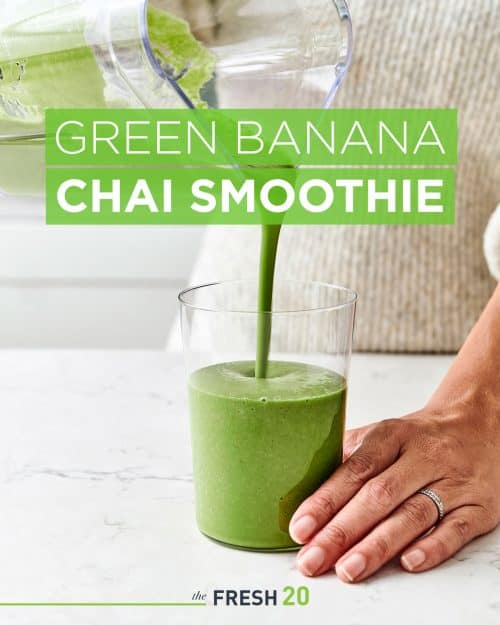 Woman pouring green banana chai spice superfood smoothie into a clear glass in a white marble kitchen