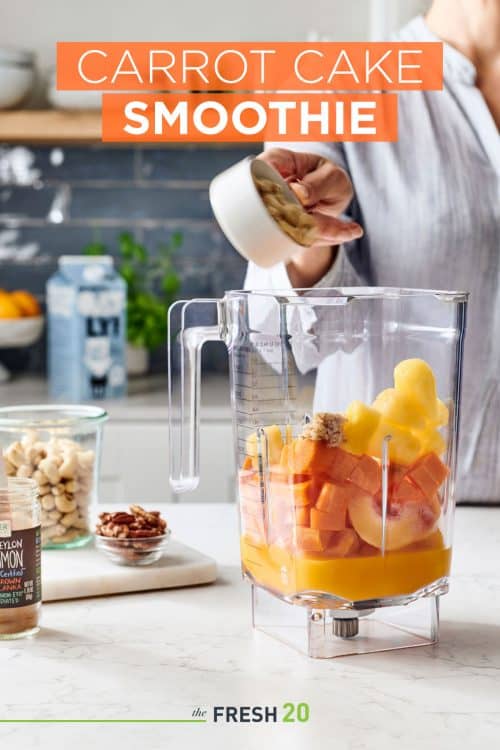 Woman pouring nuts into a blender full of carrots, peaches, pineapple & orange juice in a white marble kitchen