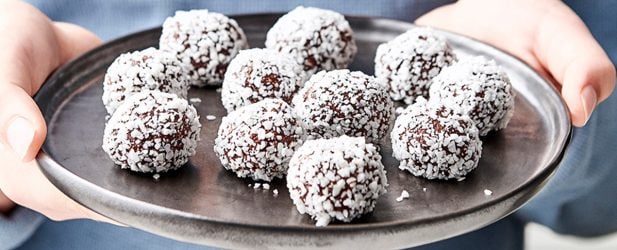 Young boy holding up a black ceramic platter of heart healthy raw chocolate truffles