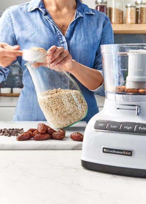 Woman scooping out oatmeal to make healthy cookies with a food processor in a modern kitchen