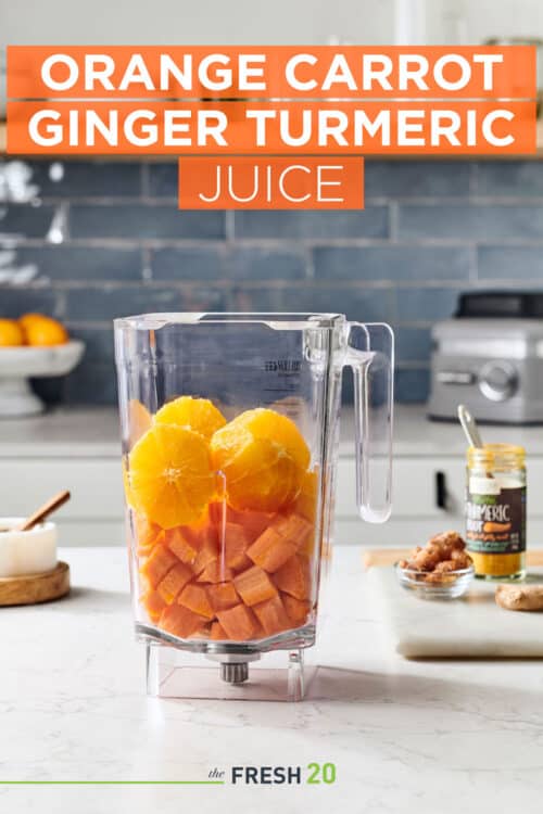 Blender full of oranges & carrots with ginger & turmeric on a white marble counter in a modern kitchen