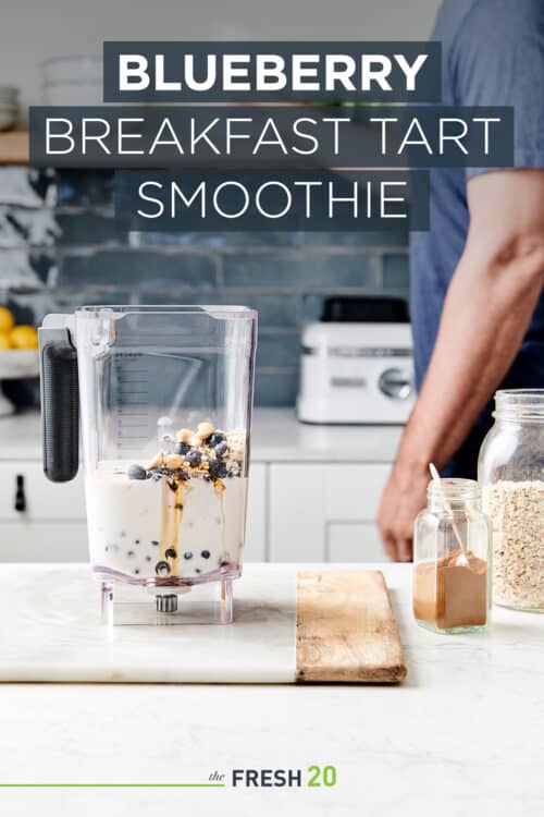 Man preparing a vegan smoothie in a blender full of creamy almond milk, honey, cinnamon and blueberries in a beautiful white marble kitchen