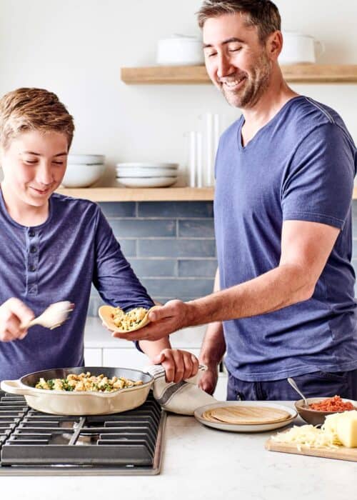 Father and son using tortillas to wrap burritos filled with egg mixture in a beautiful marble kitchen