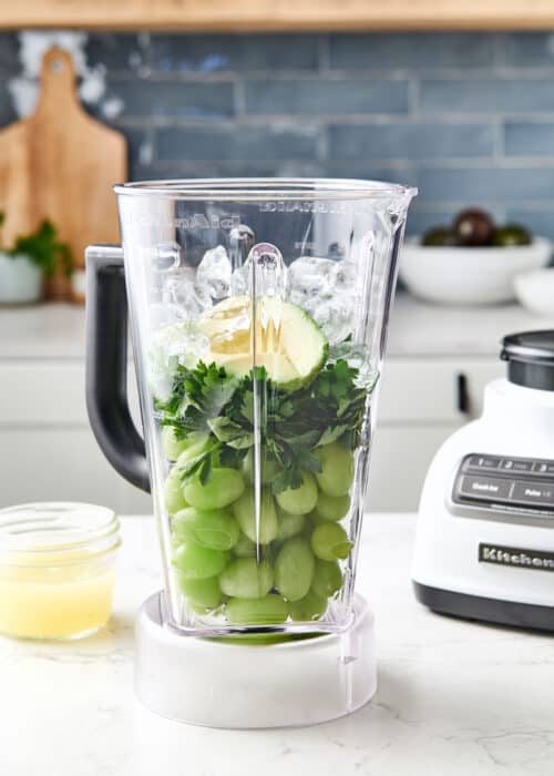 Vibrant healthy green grape parsley lemonade smoothie in a blender in a beautiful white marble modern kitchen