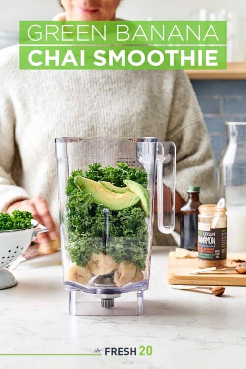 Woman making a blender full of kale, avocados, bananas & chai spices in a white marble kitchen