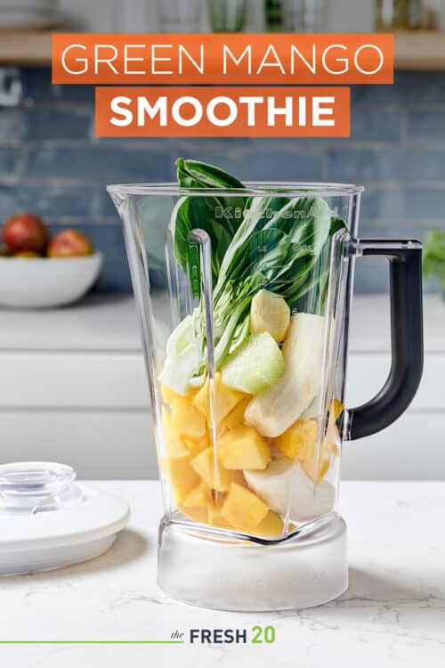 Blender full of fresh mango, bannanas, lime & bok choy in a beautiful white marble kitchen