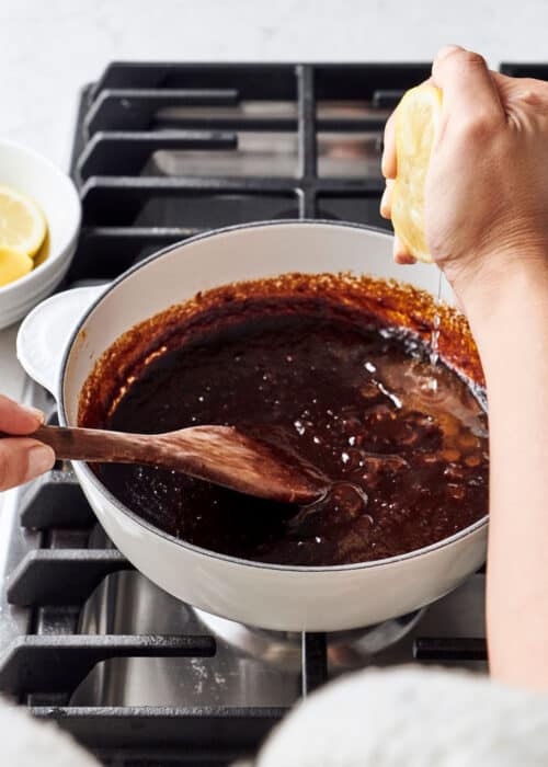 Person making homemade DIY BBQ sauce & squeezing lemon into a pot on a cooktop stove