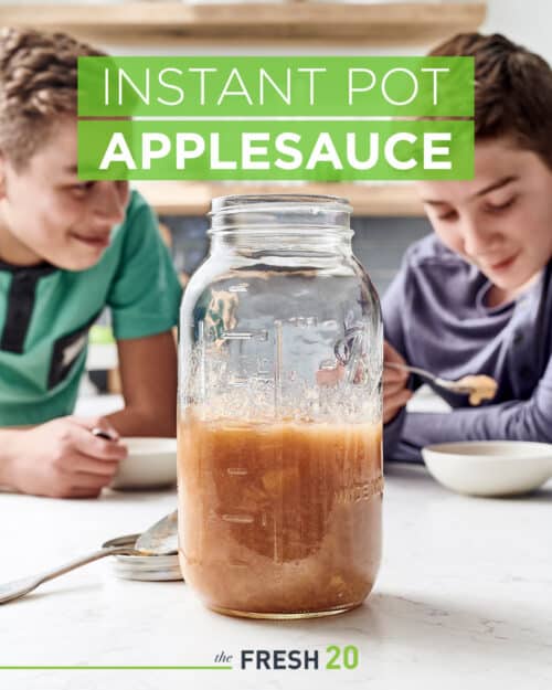 Homemade DIY Instant Pot applesauce in a masonjar with two kids eating from bowls on a white marble counter