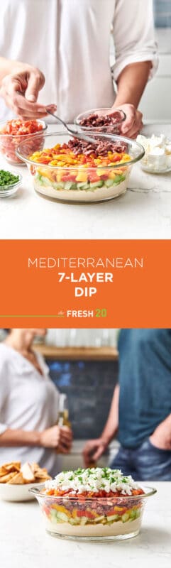 Woman using a spoon to layer olives into a serving bowl to create an easy 7-layer Mediterranean dip for entertaining