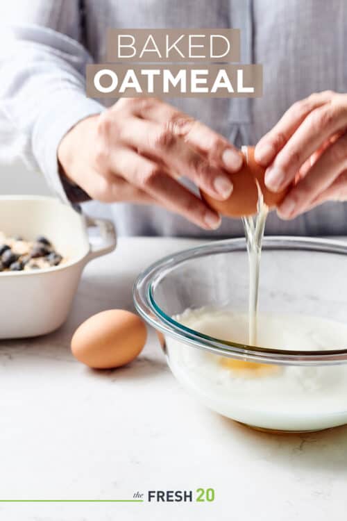 Woman cracking eggs into a glass mixing bowl filled with milk cinnamon & vanilla on a white marble surface