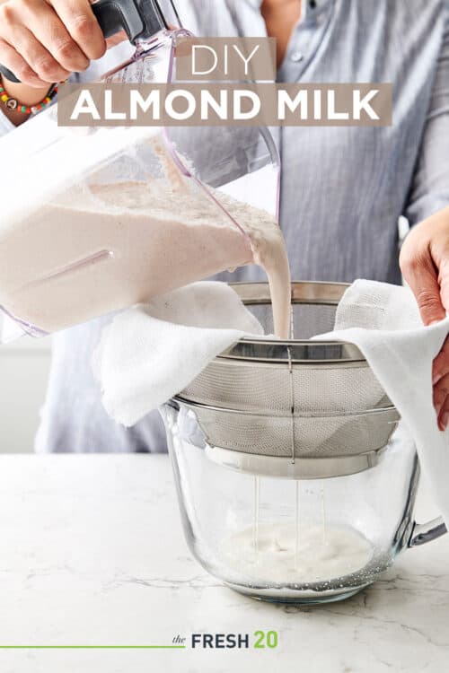 Woman pouring blended almonds into a strainer with cheese cloth to drain into a glass bowl in a white marble kitchen