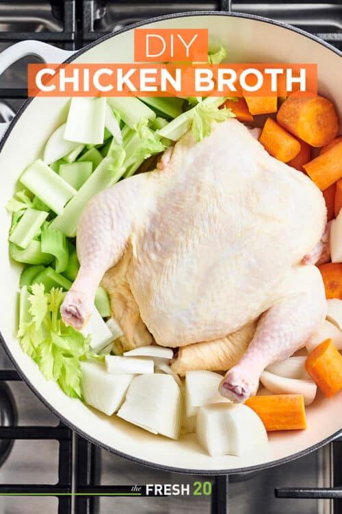 Le Creuset white Dutch oven filled with a whole chicken, fresh celery, onions and carrots on a metal cooktop