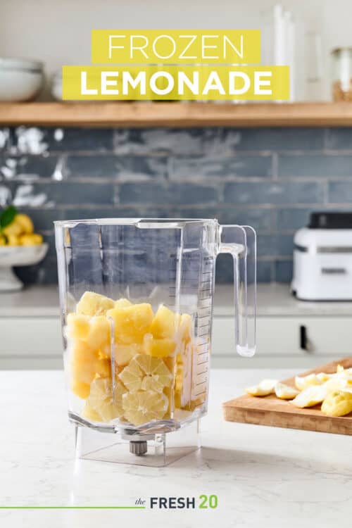 Blender full of yellow fruits such as lemons and pineapple in a beautiful marble kitchen