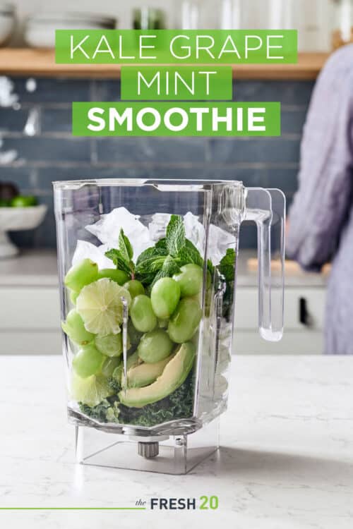 Woman filling a blender full of green grapes, mint, kale, lime & avocados in a white marble kitchen