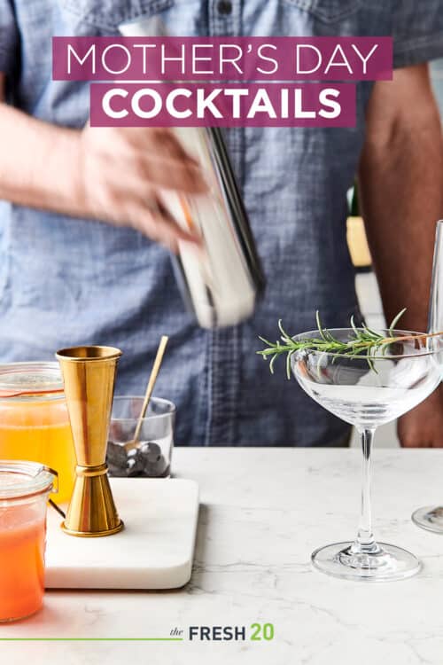 Man making Mother's Day cocktails in a shaker next to a champagne glass garnished with rosemary on a white marble surface