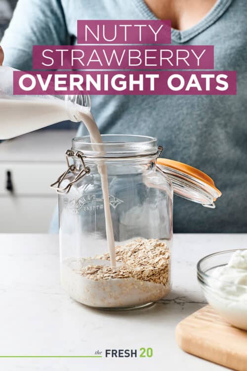 Woman pouring fresh almond milk into glass mason jar filled with oatmeal in a white marble kitchen