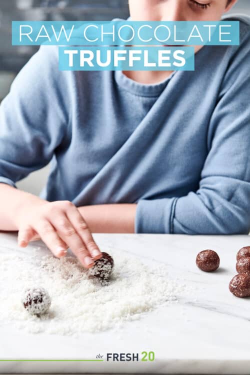 Young boy rolling heart healthy raw chocolate truffles in a pile of shredded coconut in a white marble kitchen