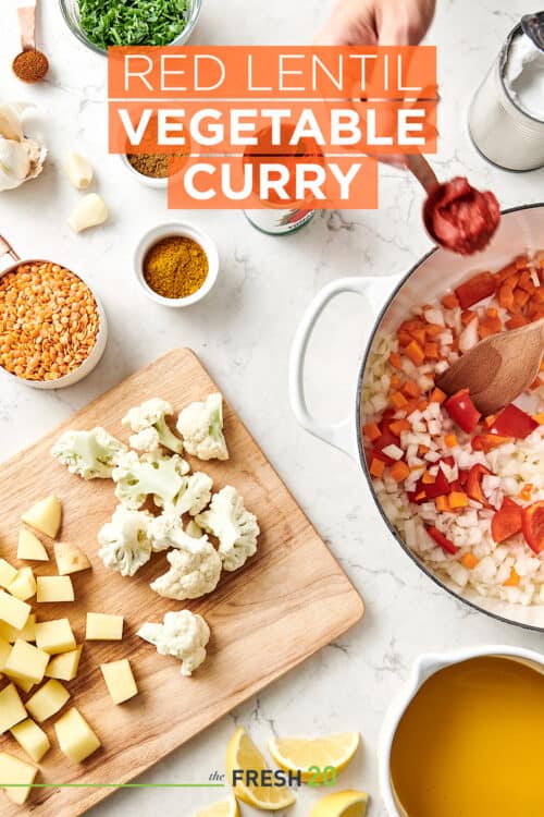 Overhead view of ingredients and spices on a wood cutting board and in a white stockpot for a vegan red lentil curry