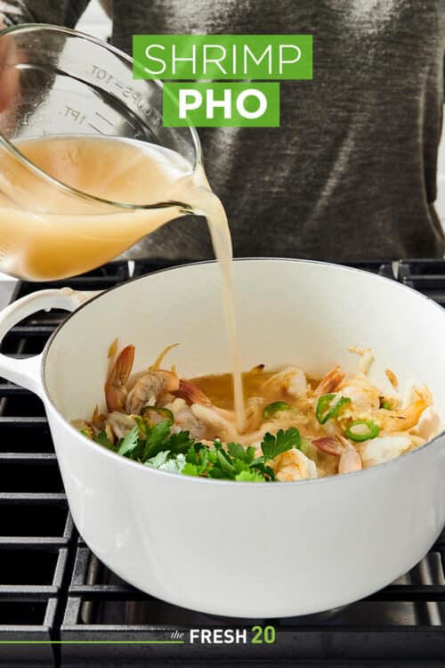 Pouring a rich resturant style broth into a Le Creuset Dutch oven filled with shrimp and other ingredients on a metal cooktop