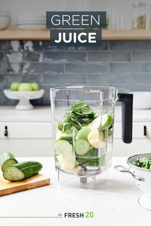 Blender full of fresh cucumber apple ginger green juice fruit & vegetables & a wood cutting board in a beautiful white marble kitchen