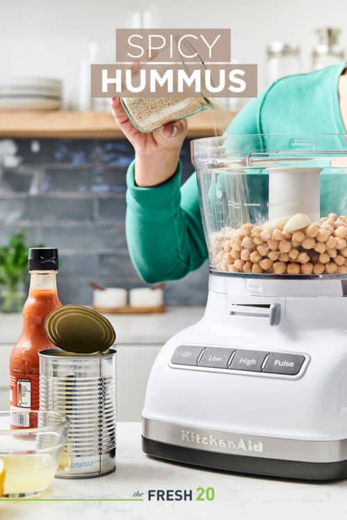 Woman filling a food procesor with garbonzo beans & other ingredients to make spicy hummus in a beautiful white marble kitchen