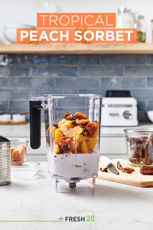 Blender on a white marble surface full of fresh and frozen fruit making tropical peach sorbet in a beautiful kitchen