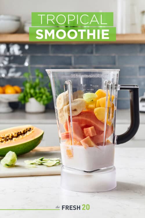 Blender full of fresh mango, banana, & papaya in a beautiful white marble kitchen