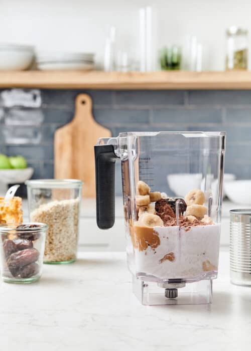 Cacao peanut butter & banana in a blender with mason jars full of dates and oats in a beautiful modern kitchen