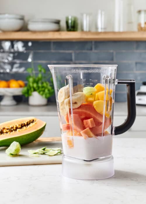 Blender full of fresh mango, banana, & papaya in a beautiful white marble kitchen