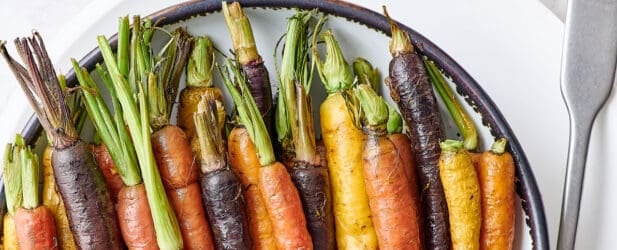 Colorful orange yellow and purple roasted carrots with their tops in a ceramic bowl