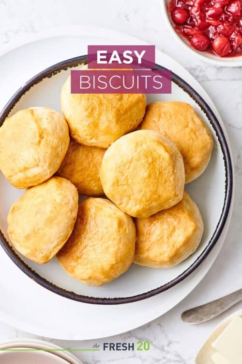 Ceramic bowl full of easy golden brown fluffy biscuits with cranberry sauce on white marble