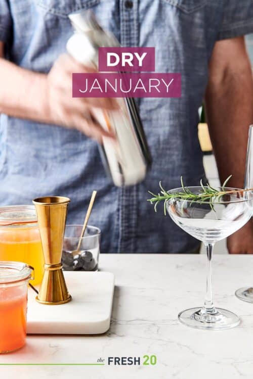 Man making Mother's Day cocktails in a shaker next to a champagne glass garnished with rosemary on a white marble surface